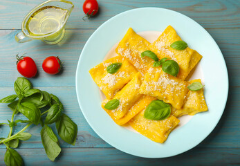 Delicious ravioli with cheese and basil served on light blue wooden table, flat lay