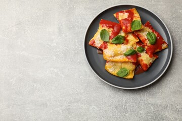 Delicious ravioli with tomato sauce, parmesan cheese and basil on grey table, top view. Space for...
