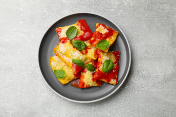 Delicious ravioli with tomato sauce, parmesan cheese and basil on grey table, top view