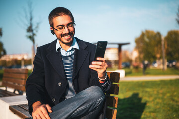 Fototapeta premium Business professional man smiling during a video chat on his smart device while relaxing at the city park.