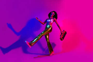 Young stylish woman dancing in vibrant neon lights holding a retro boombox, showcasing a trendy...