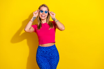 Fashionable young woman posing with sunglass on vibrant yellow background emphasizing trendy summer style