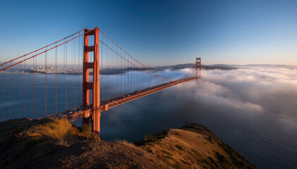 Obraz premium Golden Gate Bridge rises majestically above the fog, with San Francisco's skyline visible in the distance during early morning light