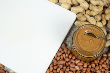 Peanut butter in a jar among scattered peanuts, space for text.