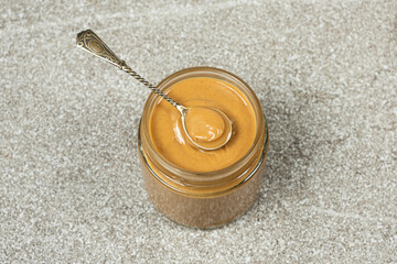 Peanut butter jar with full spoon, grey stone background