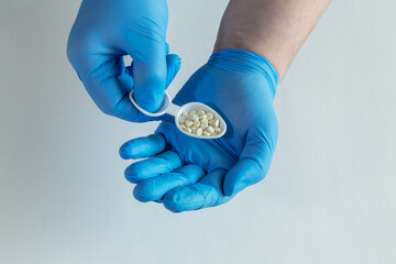 Hands in blue medical gloves holding a handful of white pills in a dosage spoon, a large dose of...