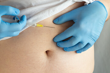 A healthcare worker's hand in a blue medical glove holding a syringe and preparing for an injection...