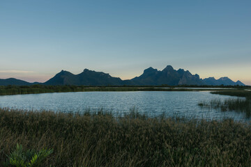 A tranquil landscape featuring majestic mountains surrounding a peaceful lake with lush greenery reflecting the calmness of nature, evoking a sense of serenity and harmony.