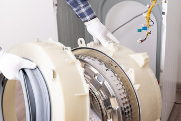 Washing machine repair process with technician handling parts indoors. A technician is carefully disassembling a washing machine drum during a repair process in service center