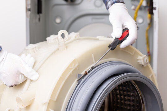Washing machine maintenance with tools and gloves for effective repair service. A technician inspects and repairs a washing machine drum using screw driver to disassemble rubber seal