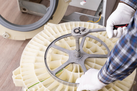 Repairing a washing machine with tools in a service workshop. A technician uses a wrench to fix a washing machine in a service workshop, focusing on the drum assembly