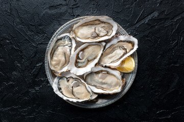 Fresh raw oysters on ice, overhead flat lay shot on a black slate background