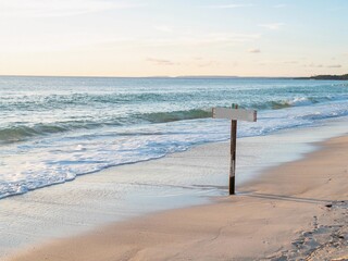 Calm beach with gentle waves at sunset, featuring a wooden signpost along the shoreline