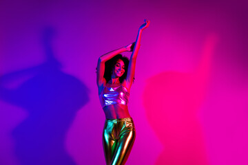 Stylish young woman dancing under vibrant neon lights, showcasing glamor and energy in a...