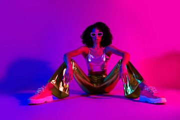Stylish young woman in vibrant neon fashion posing confidently under purple and pink lighting