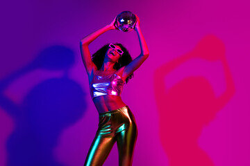 Elegant young woman posing in vibrant neon lights wearing shimmering metallic outfit during a retro...