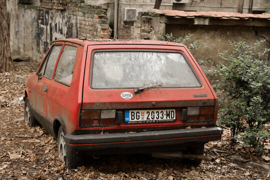 BELGRADE, SERBIA - MARCH 08, 2025: bad condition car auto YUGO Koral (Zastava Koral, Yugo 45, 55) in red color are parked outdoor. abandoned mini vehicle. Koral-55. autumn season autumnal foliage