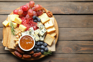 Different types of delicious cheese and other snacks on wooden table, top view. Space for text