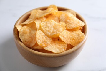 Tasty potato chips in bowl on white table, closeup