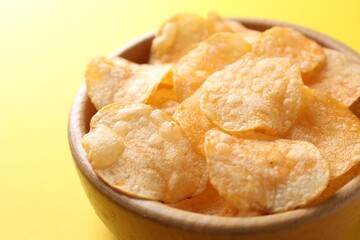 Tasty potato chips in bowl on yellow background, closeup