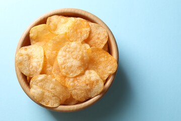 Tasty potato chips in bowl on light blue background, top view. Space for text