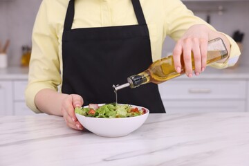 Woman pouring oil onto tasty salad at white marble table in kitchen, closeup
