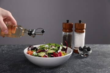 Woman pouring apple vinegar onto salad at dark textured table against grey background, closeup