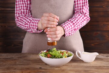 Woman salting tasty salad at wooden table, closeup