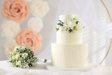 Delicious wedding cake with floral decor and bouquet on table indoors