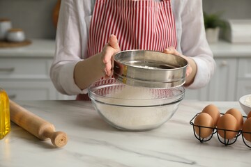 Making khinkali. Woman sieving flour into bowl at table in kitchen, closeup