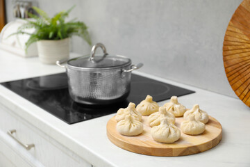Cooktop with pot and uncooked khinkali on countertop in kitchen