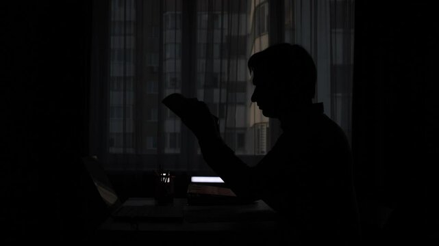 silhouette of a man in the office at his desk crumpling a document 