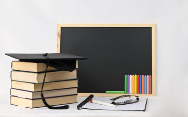 A tall stack of books, a square graduation cap, and a blackboard