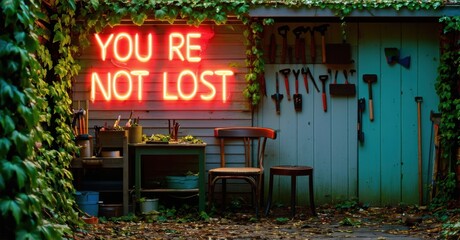 Garden shed with vibrant neon sign reading YOU RE NOT LOST. Tools hang neatly. Rustic chair, small table present. Lush greenery surrounds structure. Peaceful outdoor scene.