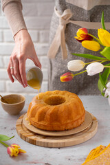 Egg liquor cake for Easter holidays. Bundt cake on a light background with tulip flowers. Easter festive food. Eierlikörkuchen in German cuisine. Food photography. Woman's hand decorating a cake  