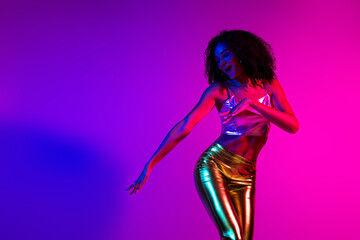 Stylish young woman dancing under vibrant neon lights in a retro-inspired environment showcasing captivating colors