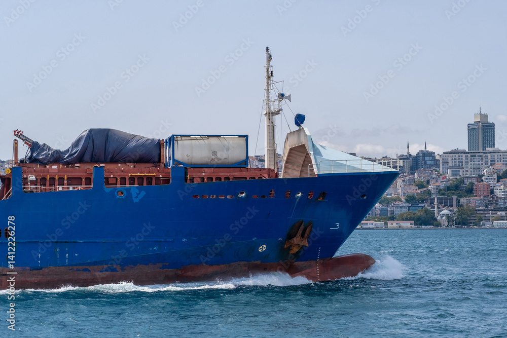 Aufkleber Cargo ship navigating through the Bosphorus with city skyline in the background during a clear day