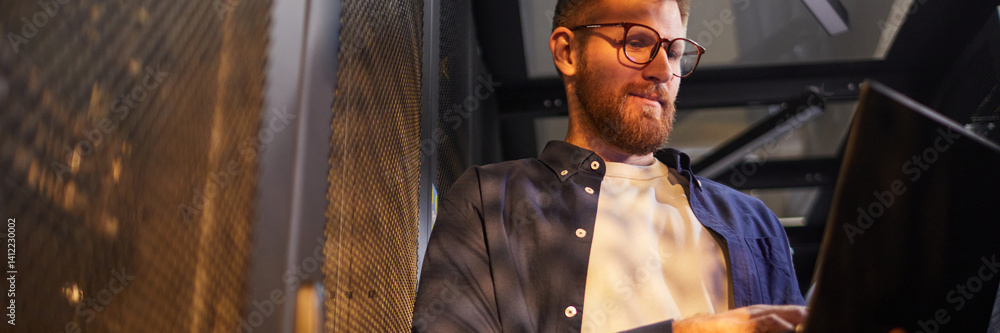 Poster website header shot of caucasian man working on a laptop by a mesh partition in a modern office envi