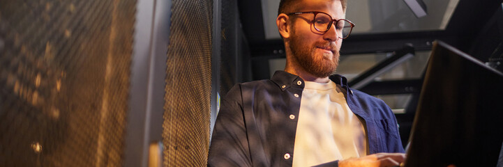 Website header shot of Caucasian man working on a laptop by a mesh partition in a modern office...