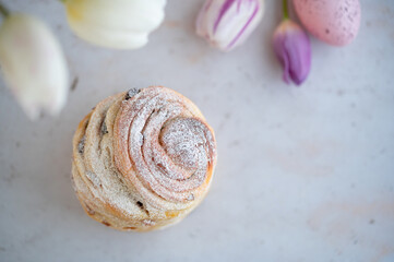 Easter Bread or Kulich with raisins. Easter yeast twisted cake Cruffin, painted eggs and tulip flowers on a stone background. Easter food.