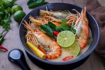 Thai style Tom Yum Kung Creamy river prawn spicy soup in black bowl on wooden background