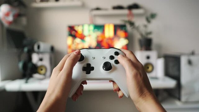Hands holding white game controller with vibrant colorful game on screen in background. Shot captures joy of home gaming, digital focus and Gen Z entertainment at stylish setup.