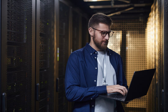 IT professional monitoring server equipment in data center holding laptop for diagnostics and system checks surrounded by racks of servers