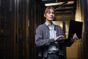 Woman standing in server room holding laptop, concentrating on her work in a high-tech environment filled with racks of servers and equipment