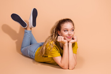 Cheerful young woman in casual outfit smiling while relaxing on beige background