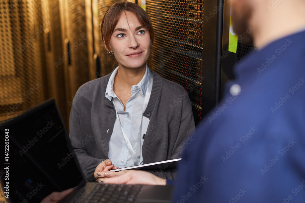 Poster smiling woman in gray cardigan holding paper while engaging in discussion with colleague in server r