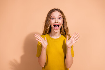 Excited young woman expressing surprise and wearing a fashionable yellow shirt against a beige...
