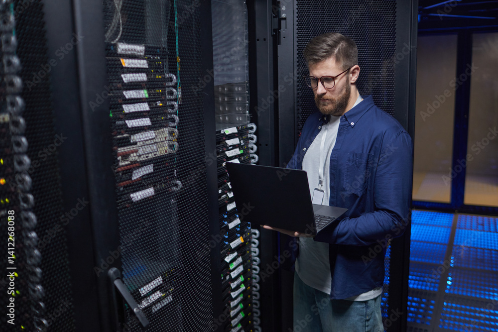 Aufkleber male it technician standing in modern server room holding laptop, checking network equipment and ens