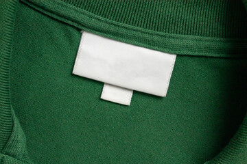 Blank white laundry care clothes label on green shirt fabric texture background