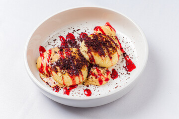 Two fluffy dumplings in a bowl, topped with fruit sauce and chocolate flakes, entice indulgence